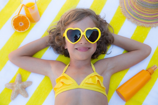 bovenaanzicht portret van meisje met een gele zonnebril en liggend op een gestreept strandlaken