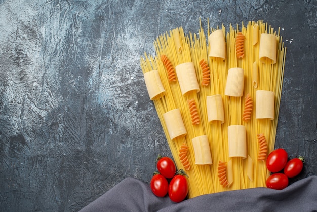 bovenaanzicht rauwe pasta's rigatoni spaghetti spiralen cherrytomaatjes paarse sjaal op grijze achtergrond met kopieerplaats