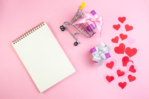 bovenaanzicht rood hart stickers happy Valentijnsdag geschreven op papier notitieblok cadeau in kleine markt trolley op roze achtergrond