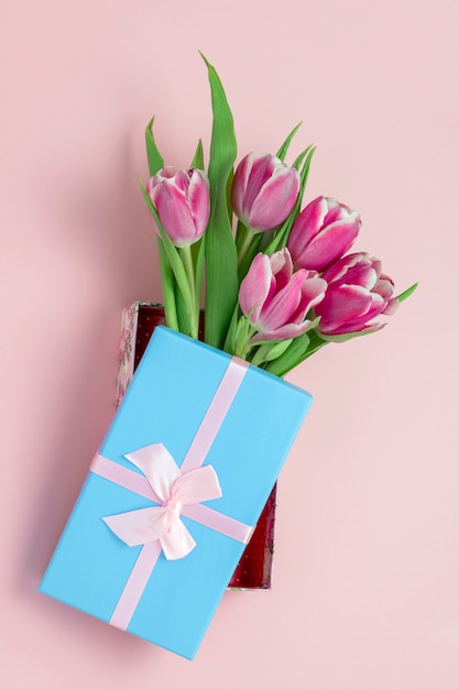 Bovenaanzicht roze tulpen in een blauwe doos met roze satijnen strik op een pastel roze