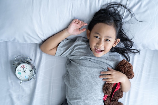 Bovenaanzicht schattig aziatisch kind klein meisje wakker en ligt in het bed met een speelgoedteddybeer