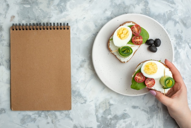 bovenaanzicht smakelijke eiersandwiches met tomaten en olijven binnen plaat wit oppervlak achtergrond lunch sandwich voedsel brood hamburger gezondheid dieet vrouwelijk