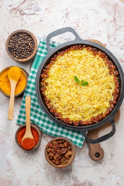 bovenaanzicht smakelijke plov in grote pan droge druiven kurkuma zwarte en rode pepers in kommen op tafel