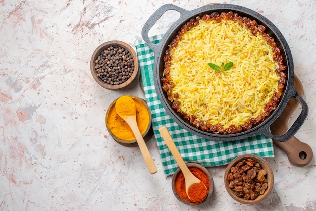 bovenaanzicht smakelijke plov in grote pan op houten bord droge druiven kurkuma zwarte en rode pepers in kommen op tafel met vrije ruimte