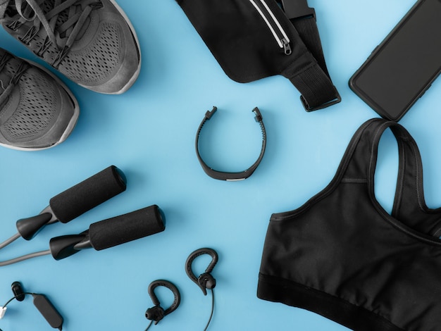 Foto bovenaanzicht sport slijtage concept met gym outfit, loopschoenen, smartphone en sport run accessoires op blauwe achtergrond met kopie ruimte.