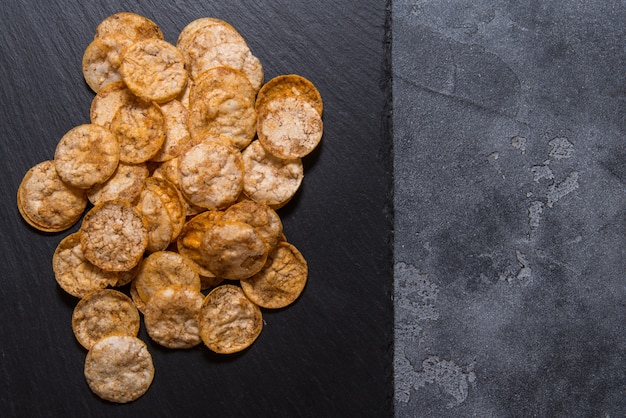 Bovenaanzicht stapel van organische, knapperige, gebakken, volkoren rijst chips met kruiden. glutenvrije gezonde snack. op zwarte gesneden stenen achtergrond