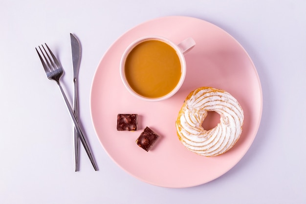 Bovenaanzicht stilleven van cake op een roze bord, bestek en kopjes met cacao of koffie met melk. selectieve aandacht, horizontale oriëntatie.
