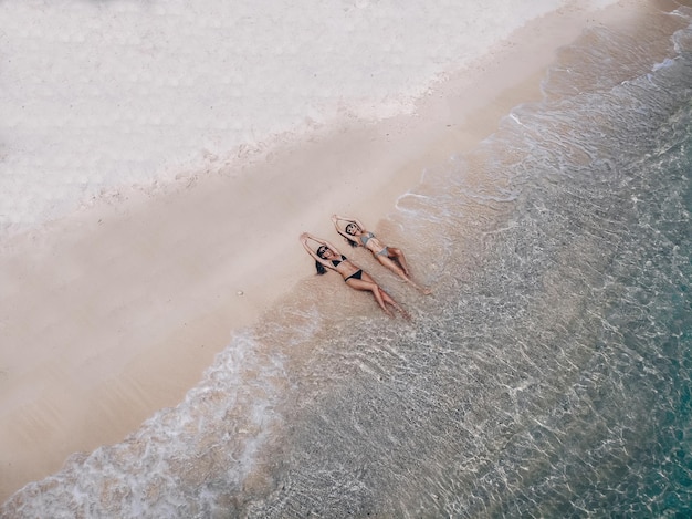 Bovenaanzicht twee jonge vrouw in een bikini liggen en ontspannen op het witte zandstrand met turquoise zeewater van Thailand, luchtfoto van drone / zomer concept