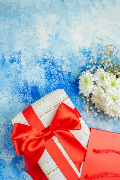 bovenaanzicht vakantie cadeau met rood lint rode papieren zak bloemen op blauwe achtergrond vrije ruimte