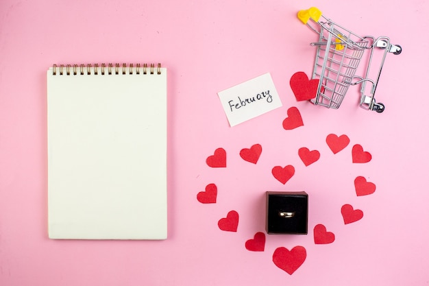 bovenaanzicht Valentijnsdag concept rood hart stickers mini trolley verlovingsring notitieboekje op blauwe tafel