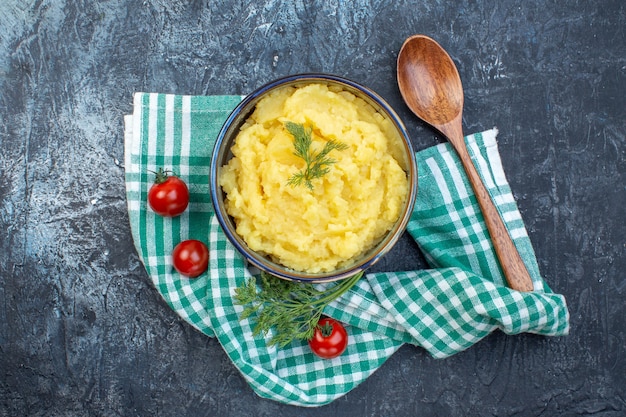 Bovenaanzicht van aardappelpuree geserveerd met dille houten lepel verse tomaten op groene gestripte handdoek op donkere kleur achtergrond met vrije ruimte