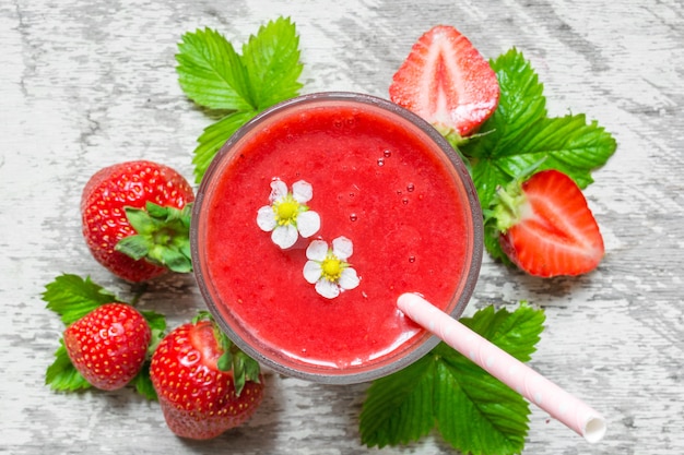 Bovenaanzicht van aardbei smoothie in een glas met stro, bloemen en verse bessen