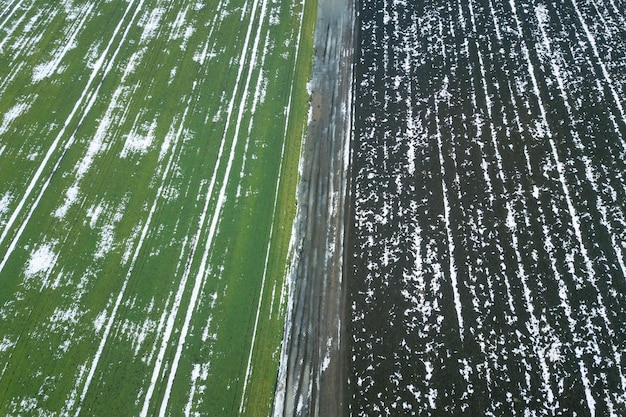 Bovenaanzicht van agrarische groene en bruine velden bedekt met sneeuw.