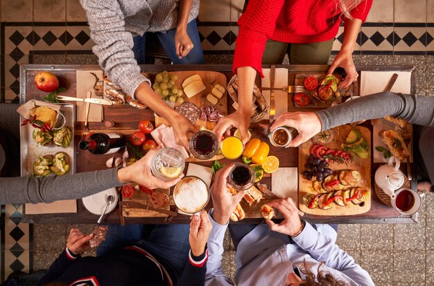 Bovenaanzicht van anonieme vrienden die een bril rammelen met alcoholische dranken terwijl ze aan tafel eten met verschillende smakelijke snacks