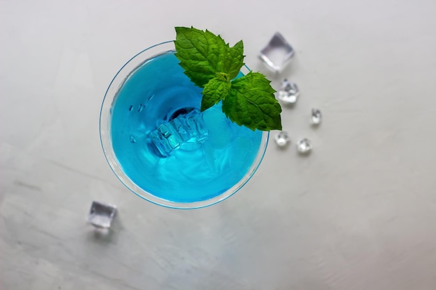 Bovenaanzicht van blauwe cocktail in martini glas met ijsblokjes en munt