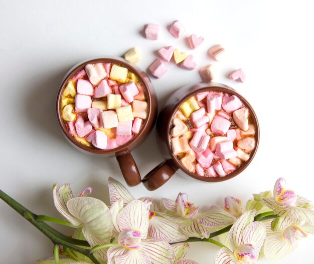 Bovenaanzicht van bruine kopjes warme chocolademelk met marshmallows in hart vorm op witte achtergrond romantische achtergrond met warme chocolademelk en orchideebloem liefde concept voor Valentijnsdag of bruiloft