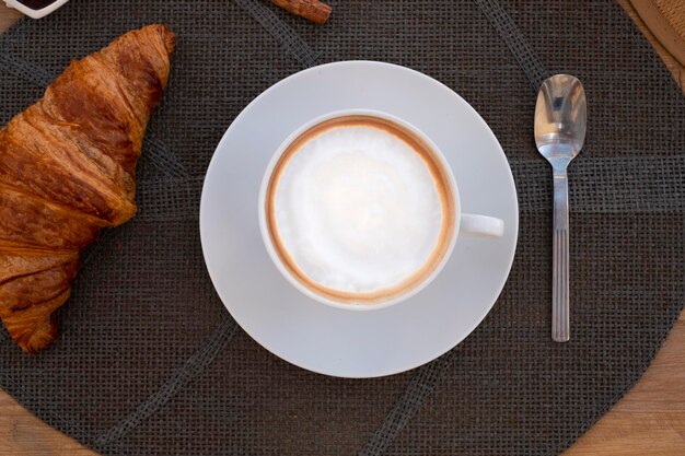 Bovenaanzicht van cappuccinokopje met melkschuim en verse croissant op houten tafel