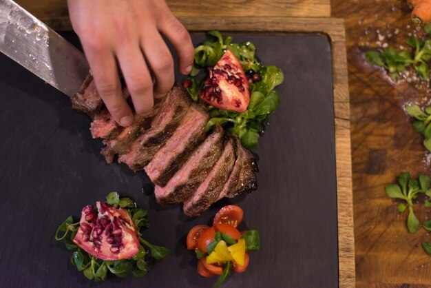 bovenaanzicht van chef-kok handen in hotel of restaurant keuken bereiden biefstuk met plantaardige decoratie