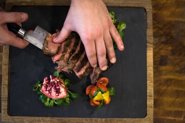 bovenaanzicht van chef-kok handen in hotel of restaurant keuken serveren biefstuk met plantaardige decoratie