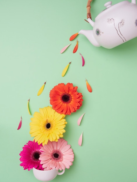 Bovenaanzicht van creatief ontwerp theepot kleurrijke bloemblaadjes gieten over bloemen op witte theekopje op lichtgroene achtergrond Lente bloeiend concept Stilleven visuele trend