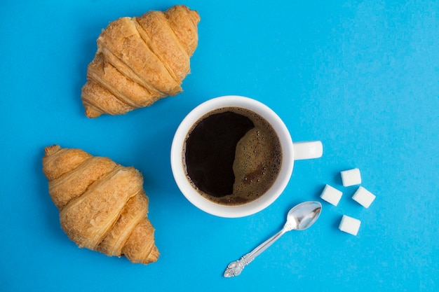 Bovenaanzicht van croissant en koffiekopje op de blauwe achtergrond. Ruimte kopiëren. Detailopname.