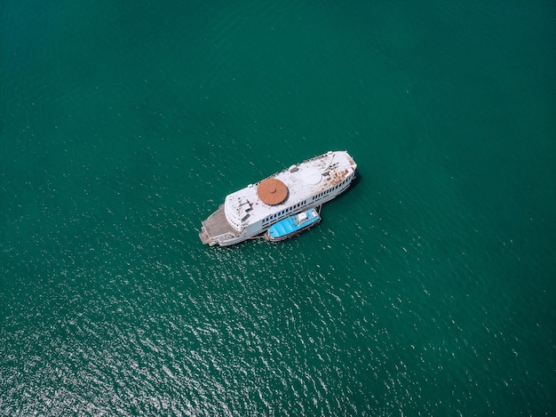 Bovenaanzicht van de grote oude roestige motorboot, houten dek, blauwe motorboot aan één kant; turquoise zee op een zonnige dag; soorten schepen.