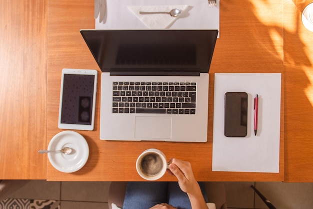 Bovenaanzicht van de handen van een meisje die haar koffie vasthouden met veel technologische objecten eromheen