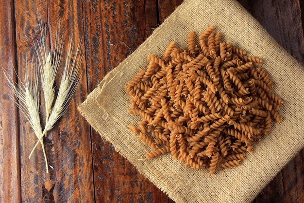 Bovenaanzicht van de hele massa van Fusilli, op stof, ruwe handdoek, op een houten achtergrond.