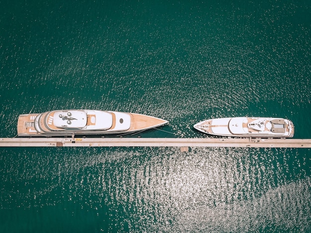 Bovenaanzicht van de luxe witte jachten afgemeerd aan de lange dunne kade, blauwe zee in een zonnige dag; miljonair concept.