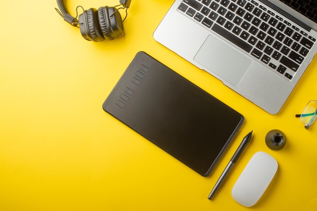 Bovenaanzicht van de ontwerper van de werkplek Creatieve ontwerper grafische tablet-laptop en accessoires voor de grafisch ontwerper Platte lay Op gele achtergrond