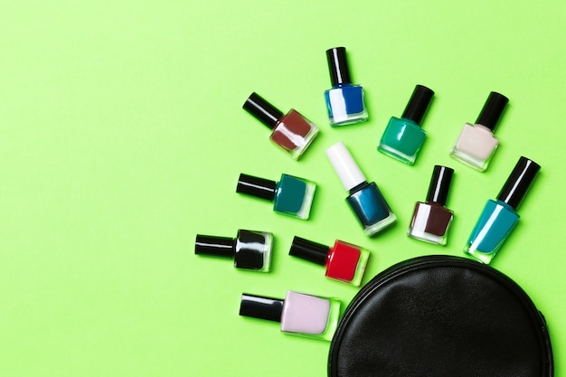 Bovenaanzicht van de set nagellakken en heldere gelvernissen die uit de cosmeticatas zijn gevallen met kopieerruimte op groene achtergrond. trendy nagelconcept.