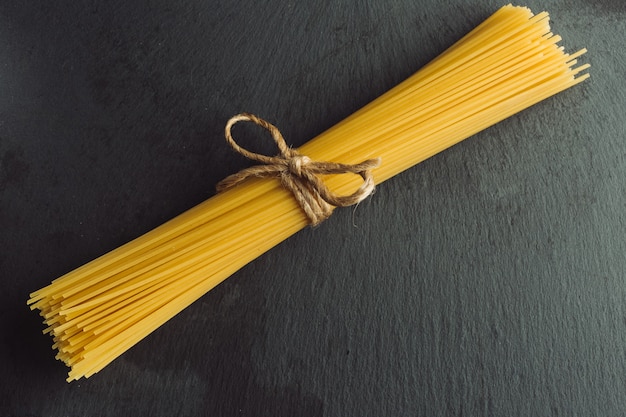 Bovenaanzicht van de spaghetti pasta vastgebonden in een bos met touwboog liggend op het zwarte leisteen oppervlak