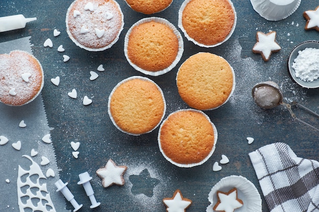 Bovenaanzicht van de tafel met suiker bestrooide muffins, fondantjesuikerglazuur en kerststerkoekjes op donkergroen hout