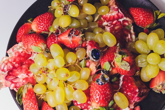 Bovenaanzicht van de twee witgouden trouwringen en een verlovingsring met diamanten geplaatst op de twee rode aardbeien.