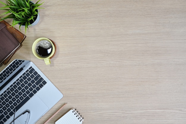 Bovenaanzicht van de werkruimte met laptopcomputer, koffie, glazen, boeken en plantendecoratie op kantoor houten tafel.