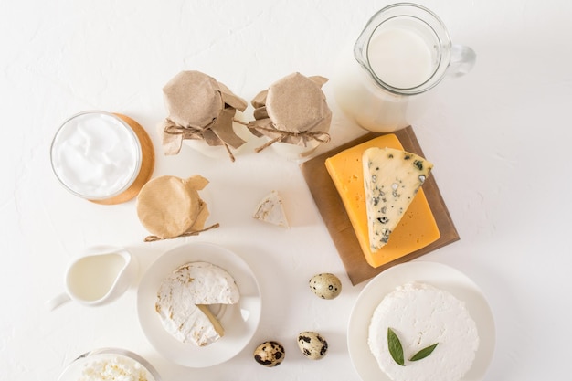 Bovenaanzicht van de witte achtergrond met verschillende zuivelproducten melk in flessen zure room kwark in de kom kaas op een houten plank