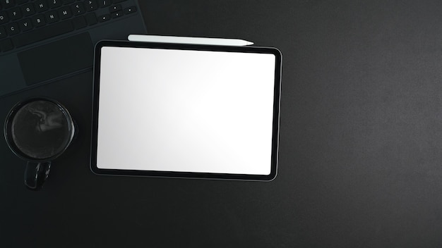 Bovenaanzicht van digitale tablet met wit scherm, koffiekopje en styluspen op zwart leer.