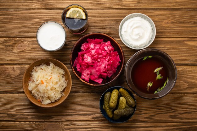 Bovenaanzicht van diverse gefermenteerde voedingsmiddelen en dranken, bronnen van probiotica geweldig voor een gezonde darm en spijsvertering: kimchi, augurken, zuurkool, miso-soep, kombucha, yoghurt, kefir, houten achtergrond