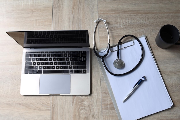 Bovenaanzicht van doktersbureautafel met laptopcomputerstethoscoopkoffie en blanco papier op klembord