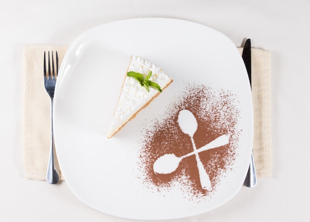 Bovenaanzicht van een artistieke plating van een plakje taart gegarneerd met room geserveerd als dessert met de contouren van twee gekruiste lepels in cacaopoeder als decoratie