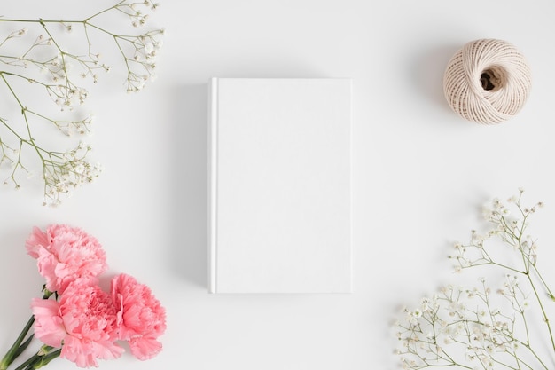 Bovenaanzicht van een boekmodel met een boeket roze anjers-werkruimteaccessoires en een gipskruid op een witte tafel