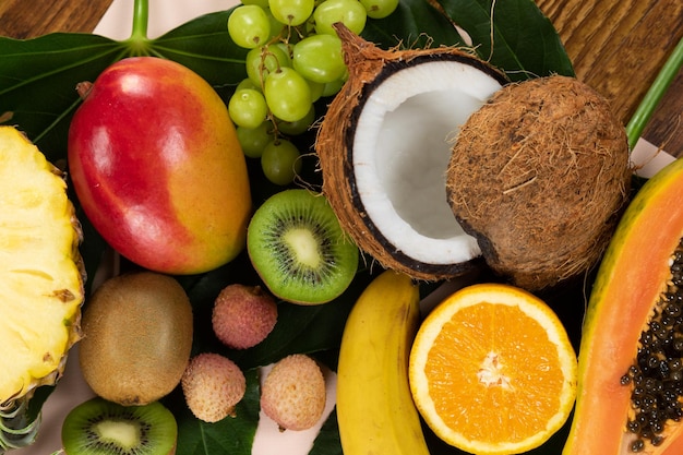 Bovenaanzicht van een compositie met een verscheidenheid aan vers tropisch fruit en groene bladeren gerangschikt op een roze oppervlak.