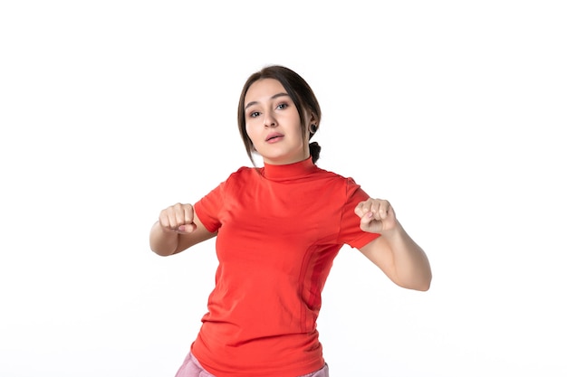 Bovenaanzicht van een gefocuste jonge vrouw die netjes haar haar verzamelt, gekleed in een oranje blouse die op een witte achtergrond staat