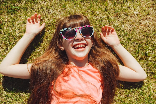 Bovenaanzicht van een gelukkig meisje glimlachend en liggend op het groene gras op een zomerdag in het park