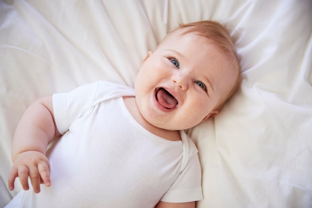 Foto bovenaanzicht van een gelukkige babyjongen die op het bed van de ouders ligt