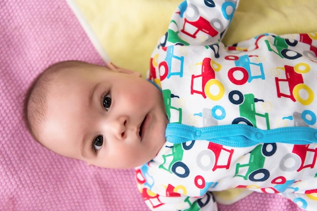 bovenaanzicht van een gelukkige, mooie pasgeboren babyjongen die op kleurrijke dekens ligt terwijl hij thuis de eerste spelletjes speelt