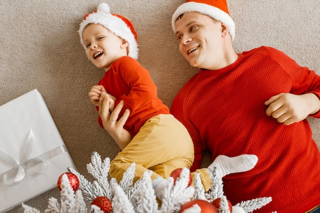 Bovenaanzicht van een gelukkige, vrolijke familievader en zoon die plezier hebben op de vloer onder de kerstboom