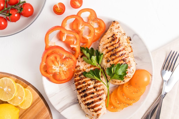 Bovenaanzicht van een grote keramische plaat met gegrilde kipfilet plakjes verse gele tomaat en peper gezond lunchmenu