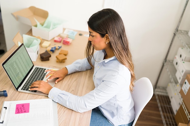 Bovenaanzicht van een hardwerkende ondernemer die bestelinformatie typt op de laptop en naar een verkooprapport van haar online winkel voor schoonheidsproducten kijkt