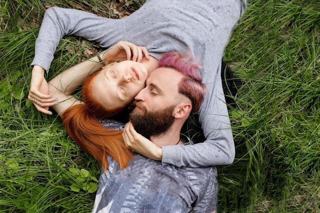 Bovenaanzicht van een hipsterpaar, zittend op een gras, zittend met gedraaide hoofden met gesloten ogen.